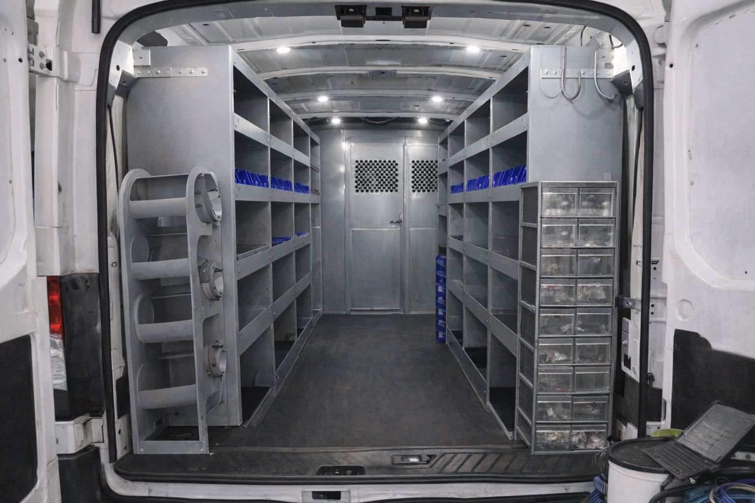 Georganiseerde metalen stellingen en ladekasten in de laadruimte van een witte bestelwagen.